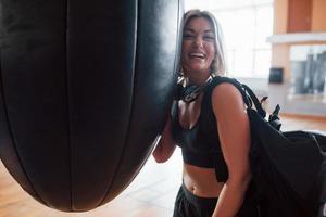 positief persoon. volwassen vrouw met zwart zak en hoofdtelefoons in de opleiding Sportschool foto