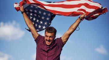 patriottisch gelukkig Mens golvend Amerikaans vlag tegen bewolkt blauw lucht foto