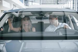 reflectie in de glas. positief manager tonen Kenmerken van de nieuw auto naar vrouw klant foto