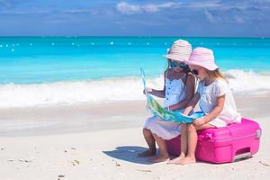 twee meisjes zittend op een koffer op een strand kijken naar een kaart