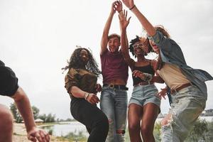 jeugd is dansen. groep van mensen hebben picknick Aan de strand. vrienden hebben pret Bij weekend tijd foto