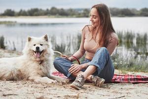 gelukkig dier. blond meisje met haar schattig wit hond hebben een Super goed tijd uitgeven Aan een strand foto