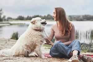 vriendschap tussen menselijk en dier. blond meisje met haar schattig wit hond hebben een Super goed tijd uitgeven Aan een strand foto