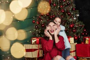 schattig weinig meisje aan het bedekken haar moeder ogen. mooi kamer met Kerstmis boom en vakantie decoratie foto