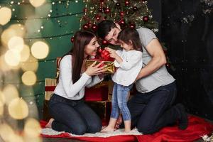 iemand is hebben Geschenk. lief familie zit in de buurt de Kerstmis boom met geschenk dozen Aan winter avond, genieten van de tijd uitgeven samen foto