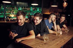 gebruik makend van telefoon. drie sport- fans in een bar aan het kijken voetbal. met bier in handen foto