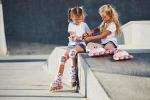 Aan de oprit voor extreem sport. twee weinig meisjes met rol skates buitenshuis hebben pret foto