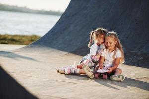 ontspannende en hebben gesprek. Aan de oprit voor extreem sport. twee weinig meisjes met rol skates buitenshuis hebben pret foto