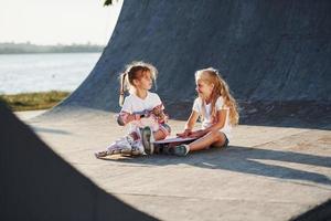 ontspannende en hebben gesprek. Aan de oprit voor extreem sport. twee weinig meisjes met rol skates buitenshuis hebben pret foto