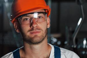 dichtbij omhoog foto. portret van ingenieur in metallurgisch fabriek in beschermend helm en eyewear foto