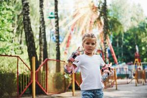 shows gebaar. vrolijk weinig meisje Aan rol skates hebben een mooi zo tijd in de park in de buurt attracties foto