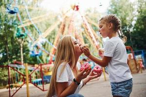 aan het eten donuts. vrolijk weinig meisje Aan rol skates en haar moeder hebben een mooi zo tijd in de park samen in de buurt attracties foto