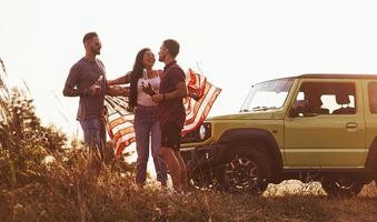 hebben gesprek. vrienden hebben mooi hoor weekend buitenshuis in de buurt van hen groen auto met Verenigde Staten van Amerika vlag foto