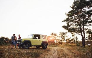 landelijk tafereel. groep van vrolijk vrienden hebben mooi hoor weekend Bij zonnig dag in de buurt van hen groen auto buitenshuis foto