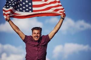 patriottisch gelukkig Mens golvend Amerikaans vlag tegen bewolkt blauw lucht foto