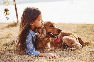 resting in de buurt de meer. schattig weinig meisje hebben een wandelen met haar hond buitenshuis Bij zonnig dag foto