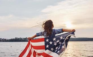verbazingwekkend zonsondergang. patriottisch vrouw kind met Amerikaans vlag in handen. tegen bewolkt lucht foto