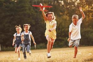 groep van kinderen hebben pret buitenshuis met rood speelgoed- vliegtuig in handen foto