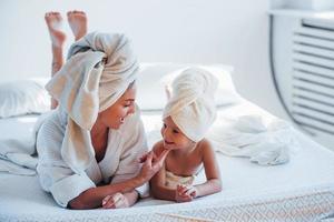 jong moeder met haar dochter hebben schoonheid dag binnenshuis in wit kamer foto