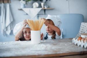 hebben pret met spaghetti. familie kinderen in wit chef uniform voorbereidingen treffen voedsel Aan de keuken foto