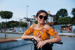 portret van positief jong meisje in zonnebril dat staat met haar fiets foto