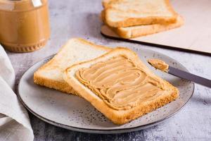 pinda boter belegd broodje Aan geroosterd brood Aan een bord en pot van boter Aan de tafel foto