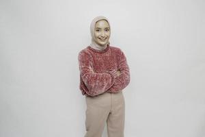 portret van een zelfverzekerd glimlachen Aziatisch moslim vrouw vervelend roze trui en hijab staand met armen gevouwen en op zoek Bij de camera geïsoleerd over- wit achtergrond foto