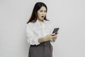 een ontevreden jong Aziatisch vrouw looks ontevreden vervelend wit overhemd geërgerd gezicht uitdrukkingen Holding haar telefoon foto