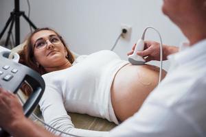 mannetje dokter doet echografie voor een zwanger vrouw in de ziekenhuis foto
