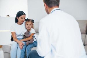 moeder met haar schattig dochter is bezoekende kliniek. luisteren naar de dokter foto