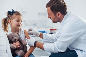 bloed bemonstering. weinig meisje met haar teddy beer is in de kliniek met dokter foto