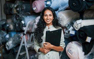 positief glimlachen werknemer met kladblok is in de opslagruimte vol van kleding foto