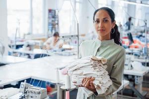 vrouw naaister staat in de fabriek met kleding in handen foto