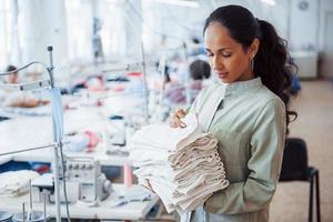 vrouw naaister staat in de fabriek met kleding in handen foto