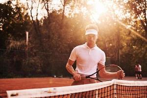 mooi zonlicht. jong tennis speler in sportief kleren is Aan de rechtbank buitenshuis foto