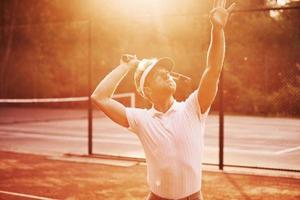 verlichte door zonlicht. jong tennis speler in sportief kleren is Aan de rechtbank buitenshuis foto