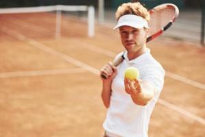 houdt bal in hand. jong tennis speler in sportief kleren is Aan de rechtbank buitenshuis foto