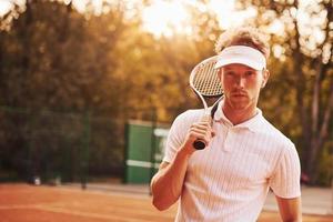 mooi zonlicht. jong tennis speler in sportief kleren is Aan de rechtbank buitenshuis foto