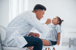 toepassingen amandel naar controleren keel. jong kinderarts werken met weinig vrouw bezoeker in de kliniek foto