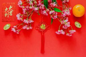 hangende hanger voor Chinese nieuw jaar ornament woord middelen rijkdom met rood envelop pakket of ang bao woord middelen auspiciën, goud ingots, oranje en Chinese bloesem bloemen Aan rood achtergrond. foto