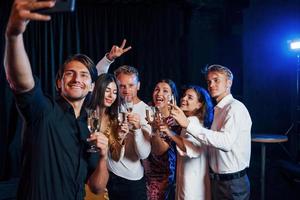 duurt selfie. groep van vrolijk vrienden vieren nieuw jaar binnenshuis met drankjes in handen foto