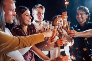 kloppen bril. groep van vrolijk vrienden vieren nieuw jaar binnenshuis met drankjes in handen foto