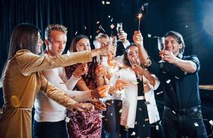 hebben pret met sterretjes. groep van vrolijk vrienden vieren nieuw jaar binnenshuis met drankjes in handen foto