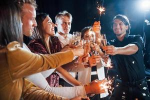 kloppen bril. groep van vrolijk vrienden vieren nieuw jaar binnenshuis met drankjes in handen foto