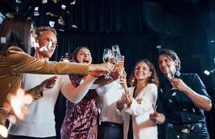 kloppen bril. groep van vrolijk vrienden vieren nieuw jaar binnenshuis met drankjes in handen foto