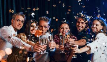 kloppen bril. groep van vrolijk vrienden vieren nieuw jaar binnenshuis met drankjes in handen foto