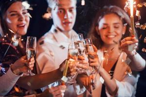 kloppen bril. groep van vrolijk vrienden vieren nieuw jaar binnenshuis met drankjes in handen foto