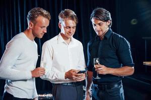 drie jongens in feestelijk kleren hebben gesprek en looks Bij de telefoon foto