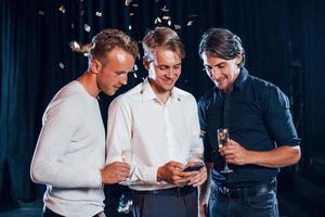 drie jongens in feestelijk kleren hebben gesprek en looks Bij de telefoon foto