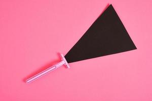 roze plastic beschikbaar scheermes en zwart papier driehoek Aan roze achtergrond foto